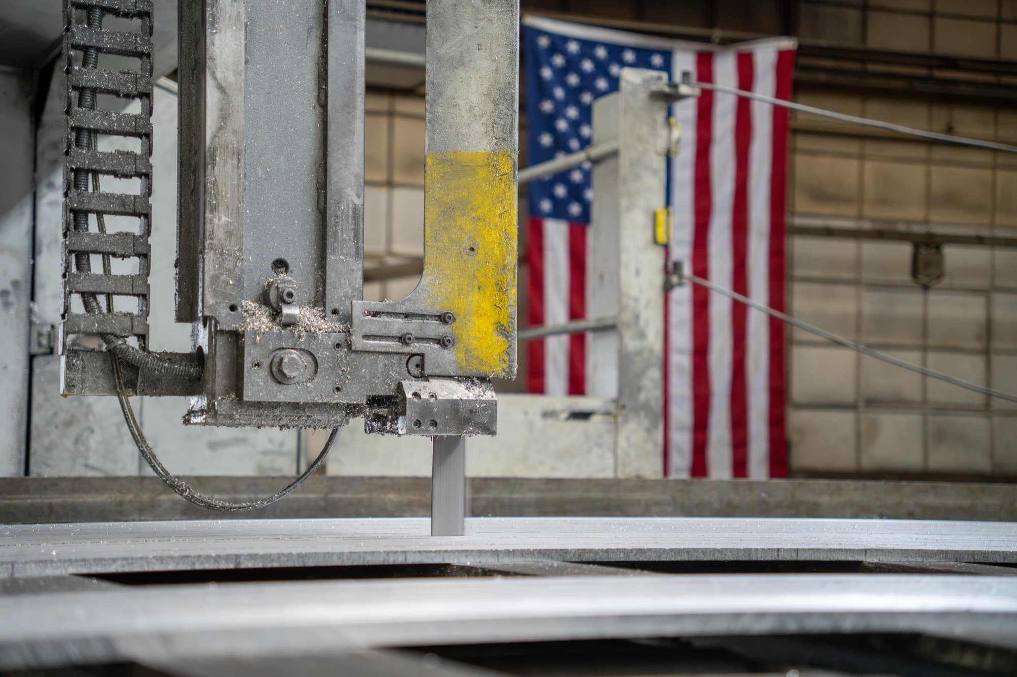 Aluminum plate on a vertical bandsaw with an American flag in the background at the NOX Metals facility