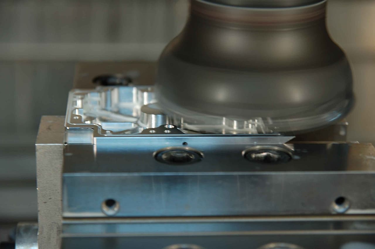 An indexable face mill cutting a machined aluminum plate part clamped down onto a fixture